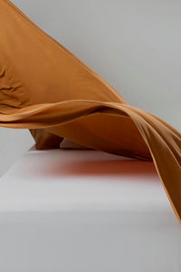 flat sheet in ginger brown floating lightly looking smooth and breathable, with a fitted sheet in white on the bed.