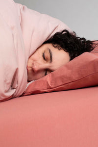 Women with curly black hair sleeping on a pink It-fits jersey fitted sheet and pillow case covered by a light pink quilt cover.