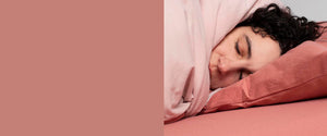 Women with curly black hair sleeping on a pink It-fits jersey fitted sheet and pillow case covered by a light pink quilt cover.