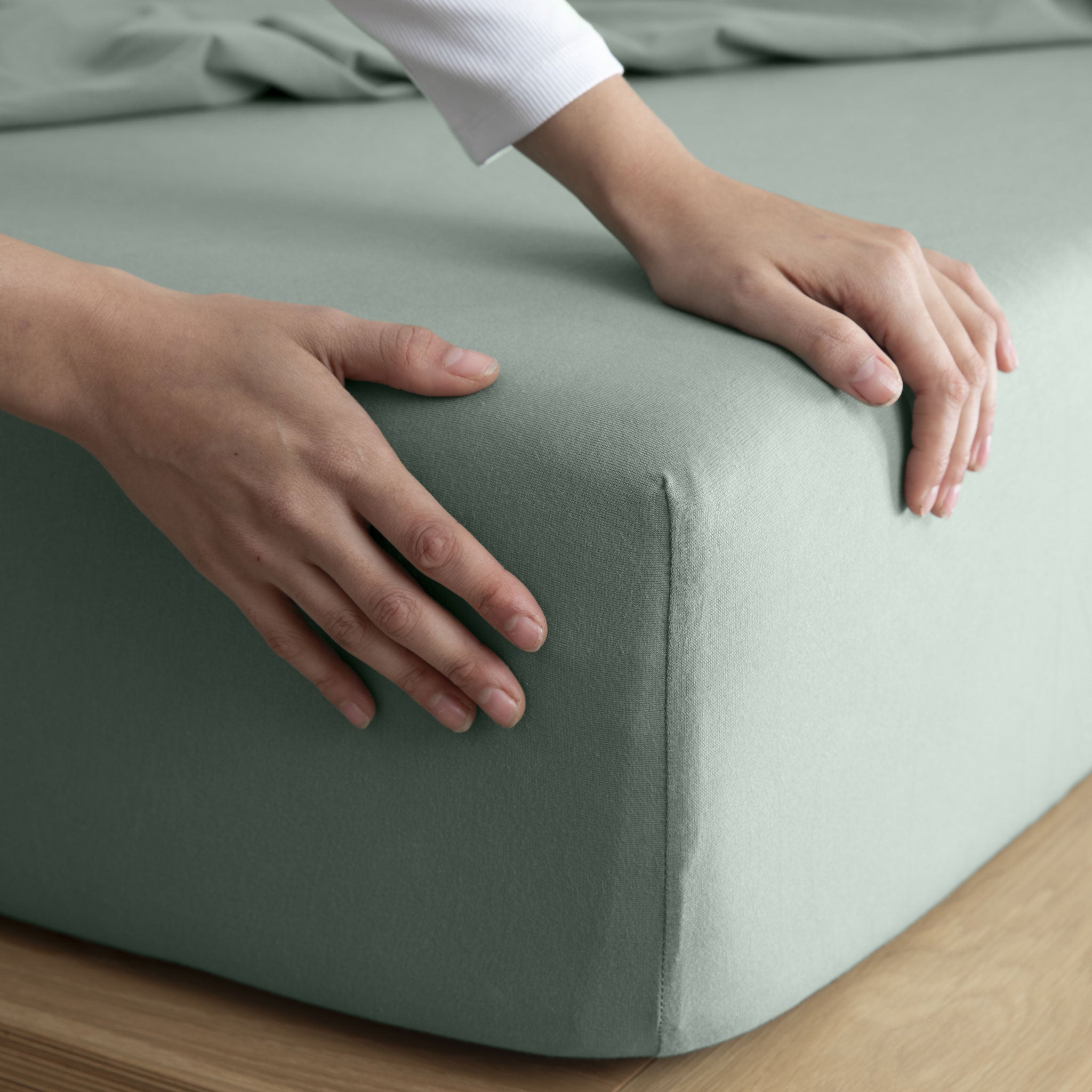 It-Fits® Sage Jersey Fitted Sheet being stretched over a mattress, showing the soft, breathable cotton fabric and perfect snug fit for comfortable bedding.