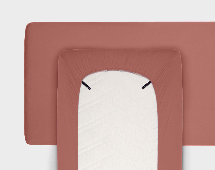 front view of the fitted sheet in vintage rose snugly fit in bed and the back view shows the unique colour-coded loops and the 360-degree elastic hem with a plain white background