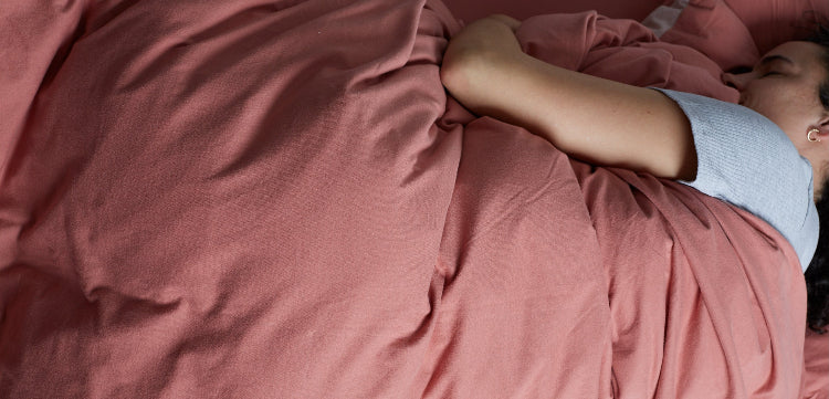 Women peacefully sleeping surrounded by soft It-fits jersey bedding. She is laying on a fitted sheet and covered by a quilt cover in pink colour.