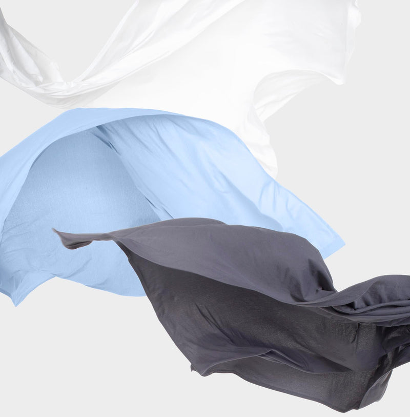 Three It-Fits® jersey cotton bed sheets in white, sky blue, and charcoal grey floating mid-air — showcasing the lightweight, breathable, and ultra-soft fabric ideal for adjustable and non-standard mattresses.